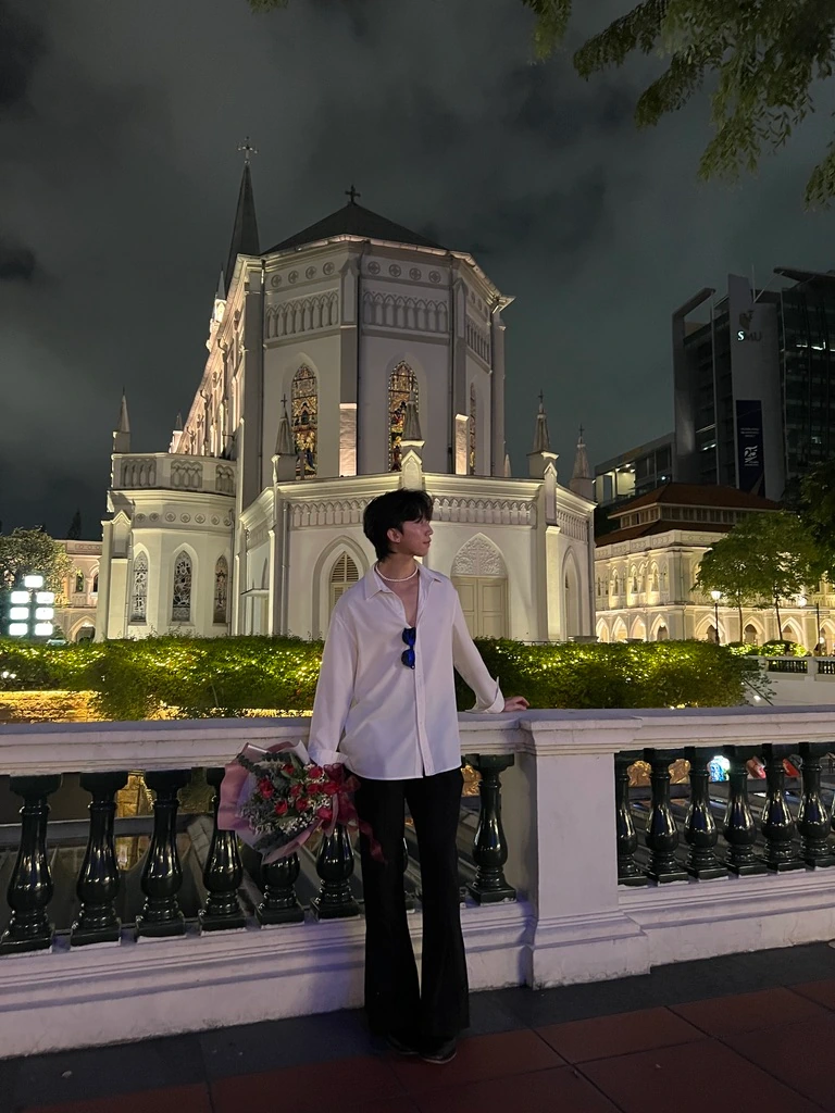Holding a bouquet beside a balustrade, with an illuminated church behind.